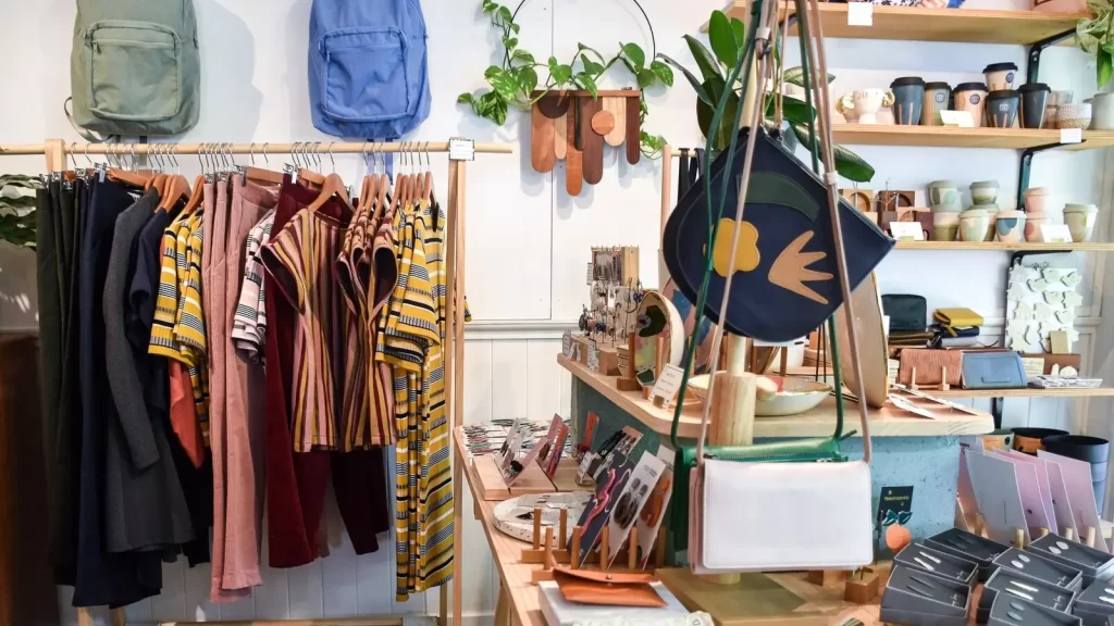 Interior of a clothing store featuring a row of clothes and a table with a hanging bag, showcasing a sustainable fashion display.